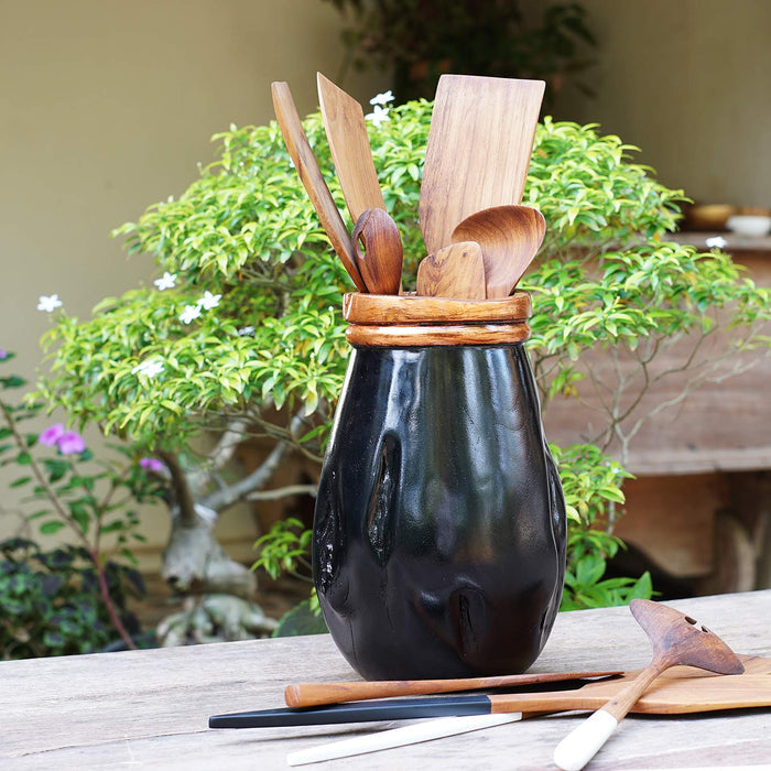 Black teak vase with copper leaf accent rim with wooden cooking utensils inside in an outside setting