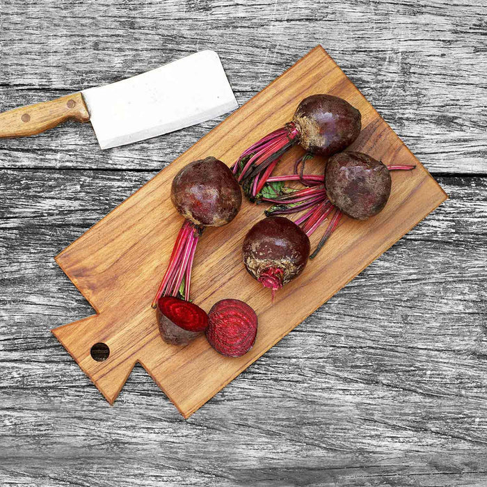 Top view of teak cutting board/serving platter with beets next to knife displayed on a wooden surface