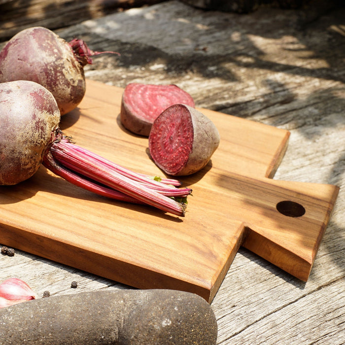 Close up of handle of teak cutting board/serving platter with beets displayed on a wooden surface
