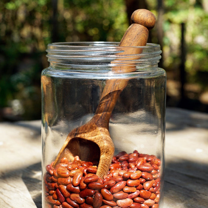 Small teak lentil scoop with long handle displayed inside a jar of lentils outside on a wooden surface