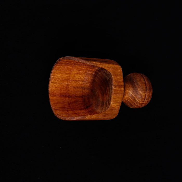 Top view of small teak lentil scoop with a short handle displayed horizontally on a black background