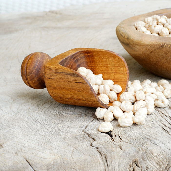 Small teak lentil scoop with short handle with scoop of lentils next to a bowl of lentils on a wooden surface