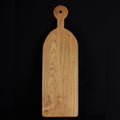 Rico & Plato sorrel teak cutting board serving platter displayed vertically on a black background