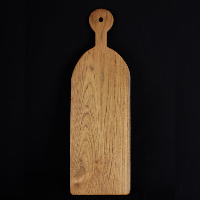 Rico & Plato sorrel teak cutting board serving platter displayed vertically on a black background
