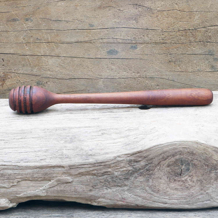 Wooden honey dipper displayed horizontally on a wooden surface