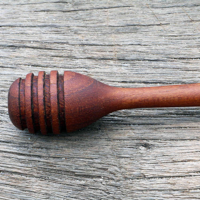 A hand-crafted wooden honey dripper with a teak finish, featuring ridges to control the flow of honey.