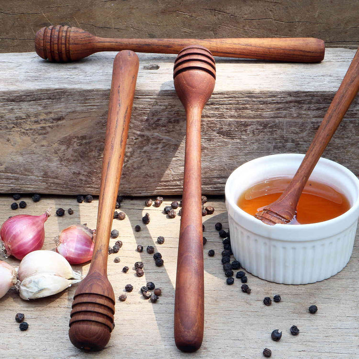 Set of 4 wooden honey dippers with bowl of honey, peppercorn, and garlic on a wooden surface