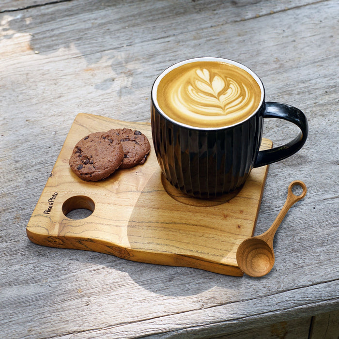 Teak coffee cup server with a mug of creamy coffee, 2 cookies, and a spoon displayed on a wooden surface