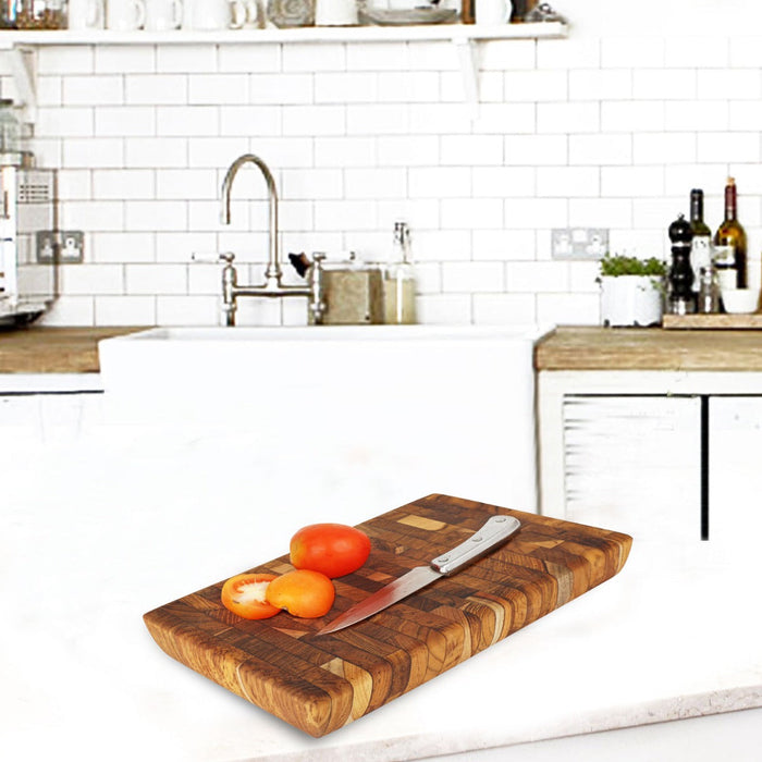Rectangular end grain teak cutting board with a knife and tomatoes placed on top displayed in a kitchen setting