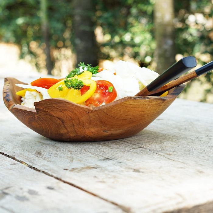 A handcrafted teak wood salad bowl with a natural edge, placed on a wooden surface, filled with salad.