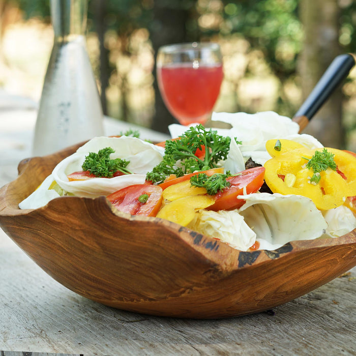 Teak salad fruit bowl with veggies and fruit inside the bowl with drinks in the background on a wooden surface