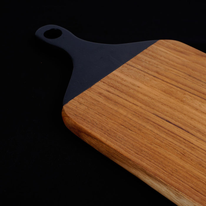 Close up of black handle of a teak cutting board/serving platter displayed on a black background