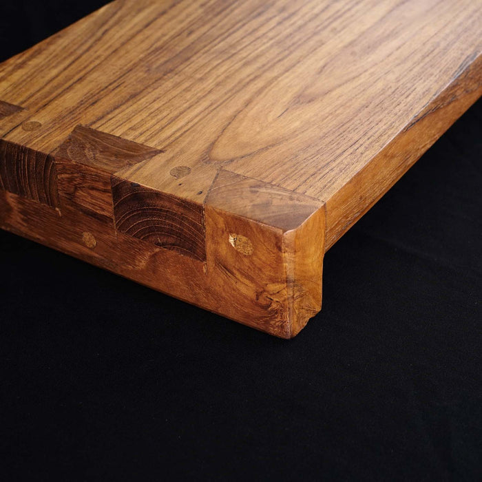 Close up of corner of Rico & Plato wasabi teak serving platter displayed on a black surface