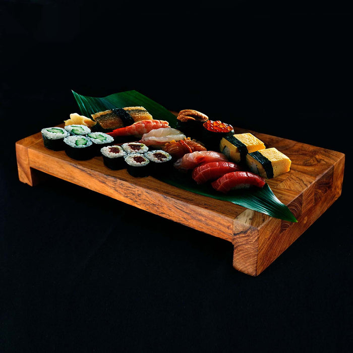 Rico & Plato wasabi teak serving platter with an assortment of sushi on top displayed on a black surface