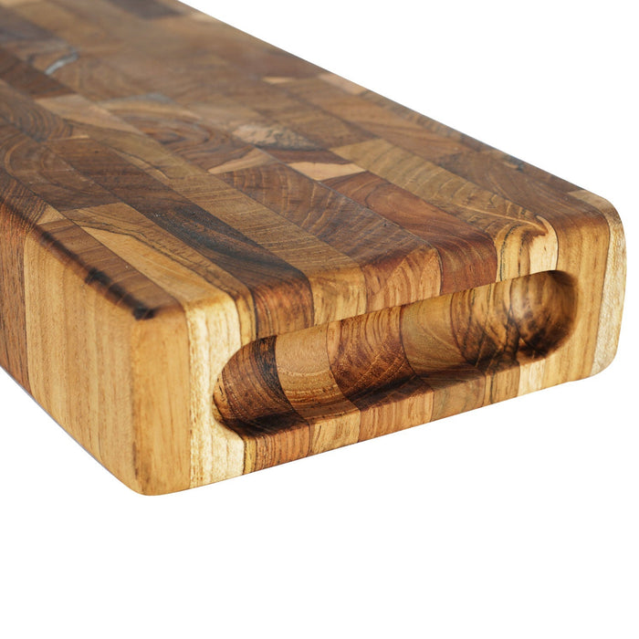 Close up of carved out handle of rectangular end grain teak cutting board displayed on a white background
