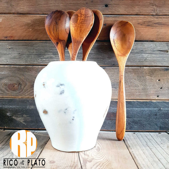 Four teak wood spoons in a white vase with a teak wood spoon placed by it  with a wooden background