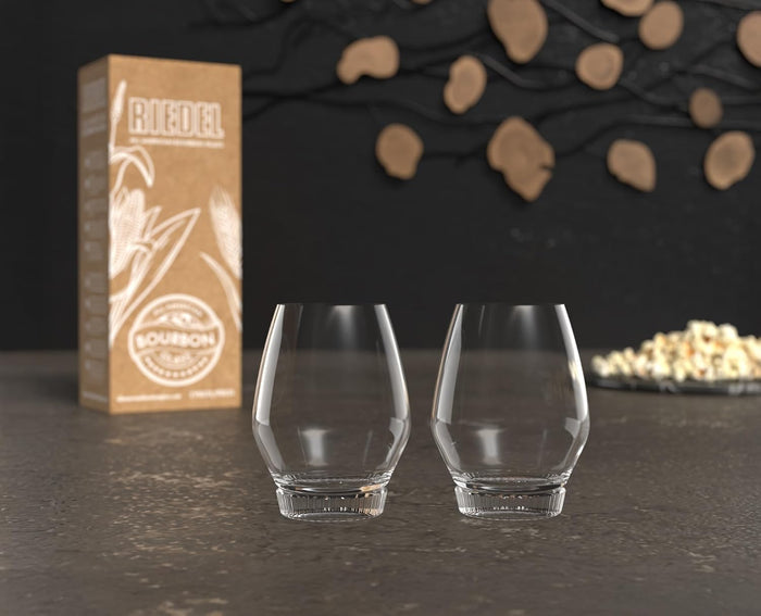 Two clear glass tumblers with a box labeled 'Bourbon' on a dark surface.
