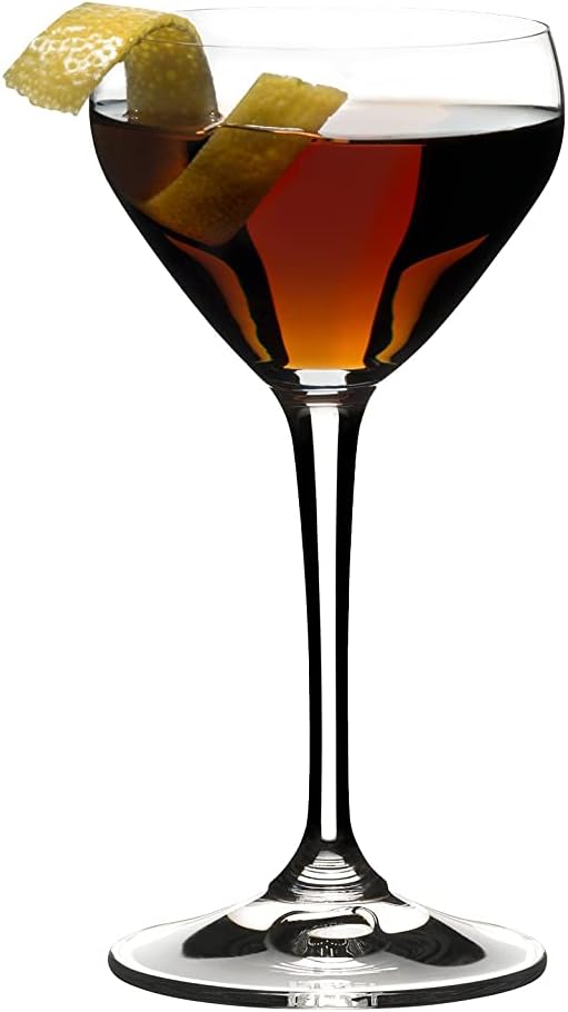 Riedel drink specific glassware Nick & Nora cocktail glass with brown liquid and lemon peel inside on a white background