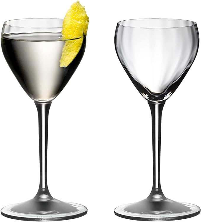 Set of two Riedel drink specific glassware Nick & Nora one with a white liquid and lemon peel inside and other is empty on a white background