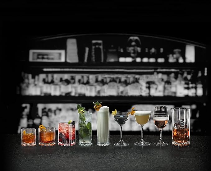 An assortment of Riedel drink specific glassware on a black surface and bar background