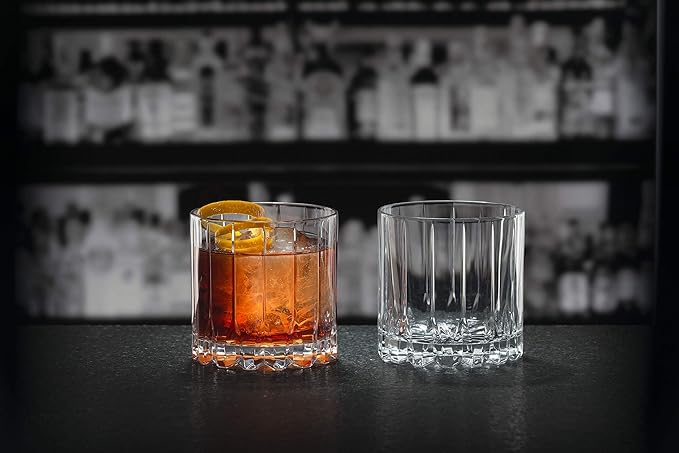 Set of two Riedel rocks glasses one with brown liquid and other empty on a black surface and bar background