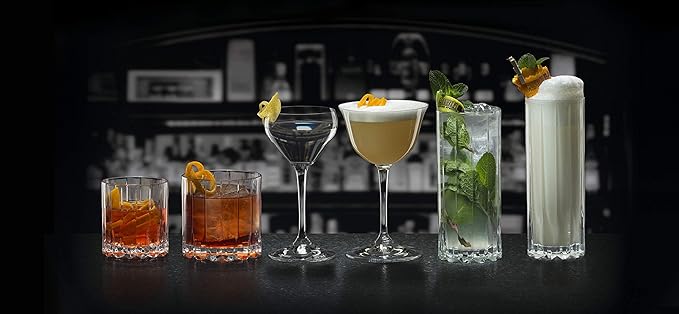 An assortment of Riedel drink specific glassware on black surface and a bar background
