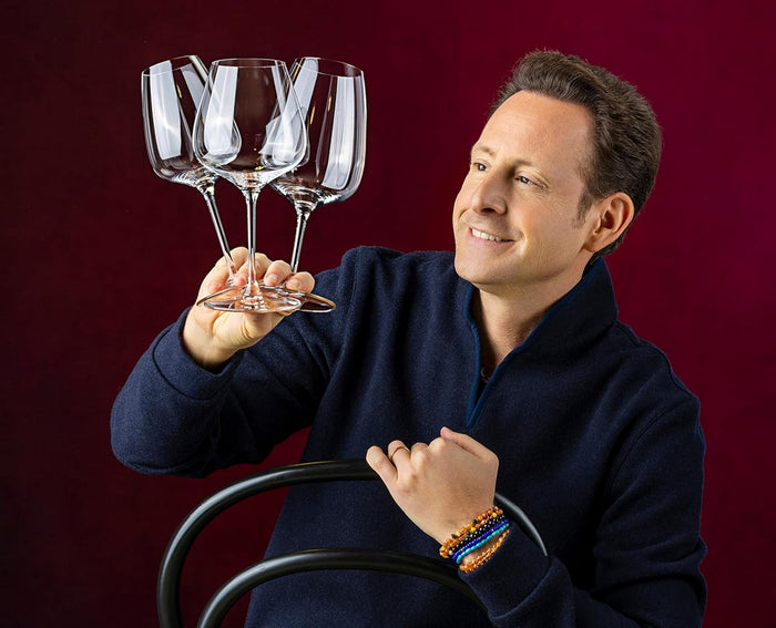Man holding three wine glasses against a red background