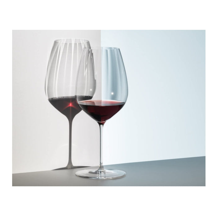 Riedel performance cabernet merlot glass with red wine inside on a reflective surface on a white background