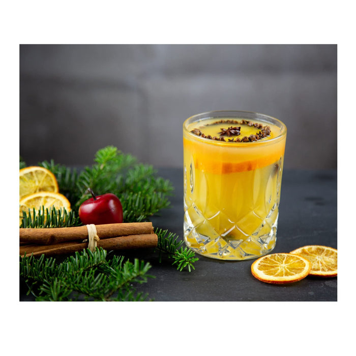 Riedel fine crystal tumbler spey whisky with a cinnamon and orange drink inside next to sliced oranges, cinnamon sticks, a cherry, and pine tree branches on a black surface