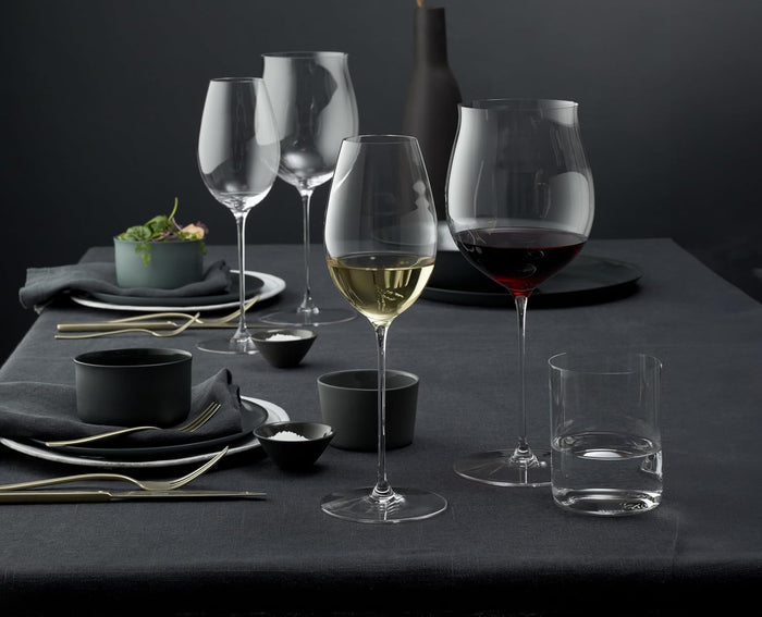 An assortment of Riedel superleggero burgundy grand glasses red and white wine inside two of the glasses on a black and gold themed dining table