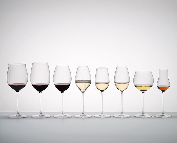 An assortment of Riedel Superleggero burgundy grand glasses with an assortment of liquids inside the glasses on a white background