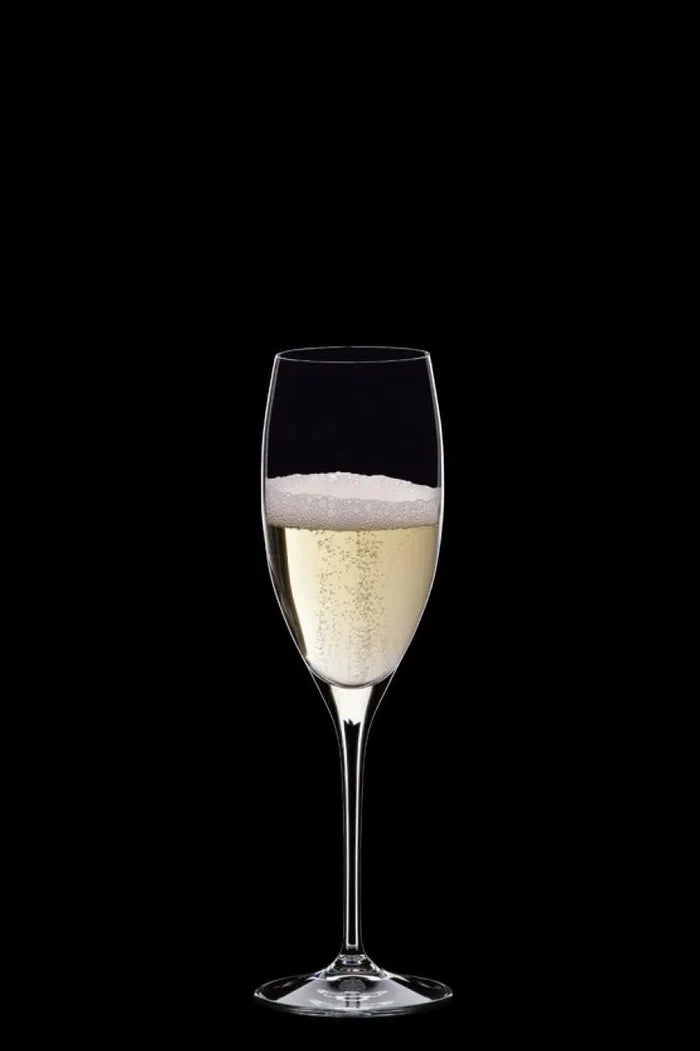 A single clear champagne flute filled with pale golden bubbly liquid, centered on a solid black background.