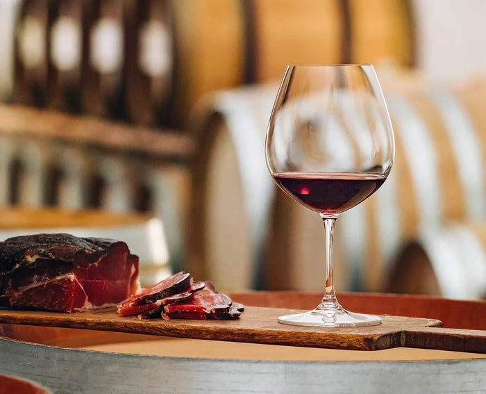 Glass of red wine on a wooden board with sliced meat, blurred background