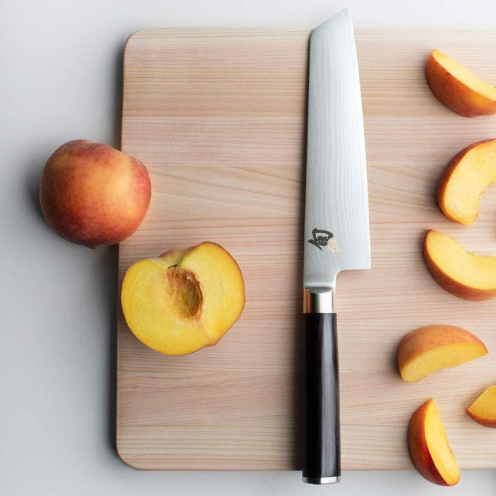 Shun Classic Master Utility 6.5″ displayed vertically next to sliced peaches on a cutting board