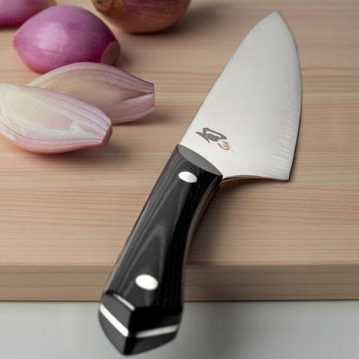 Chef knife placed next to shallots on a cutting board