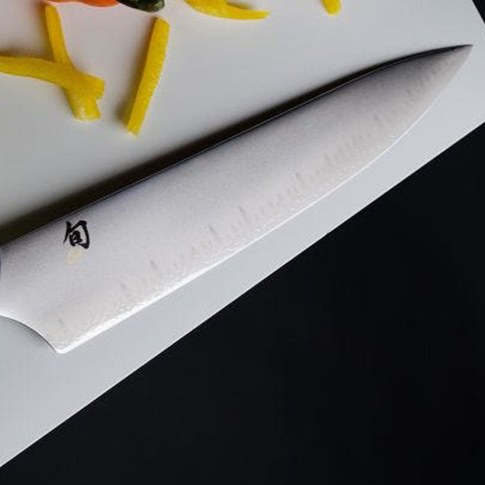 Close up of chef knife blade placed next to to sliced peppers on a white countertop