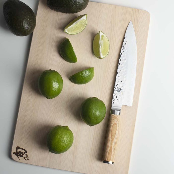 Chef knife next to limes and avocados on a cutting board displayed on a white countertop