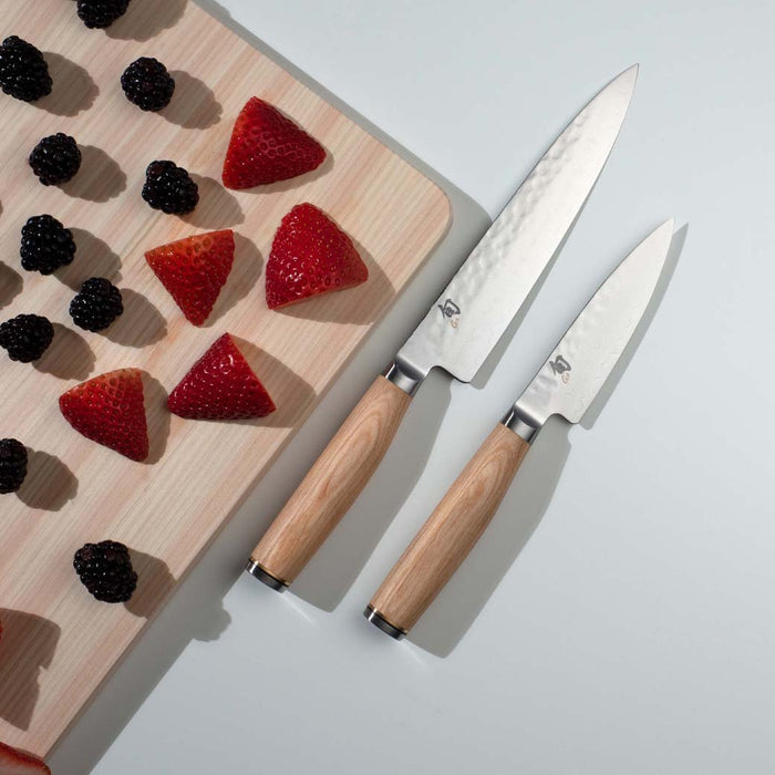 Set of 2 knives with blonde handles next to cutting board with strawberries and blackberries displayed on a white background