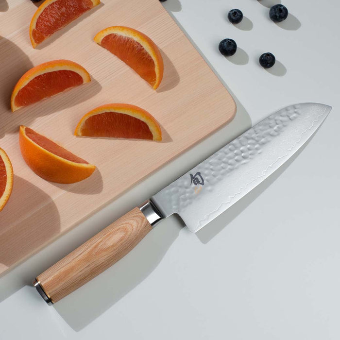 7 inch Shun Premier santoku knife with blonde handle displayed next to blueberries and sliced oranges on top of a cutting board placed on a white countertop