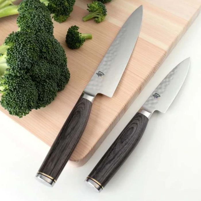 2 utility knife displayed on a cutting board next to broccoli on a white countertop