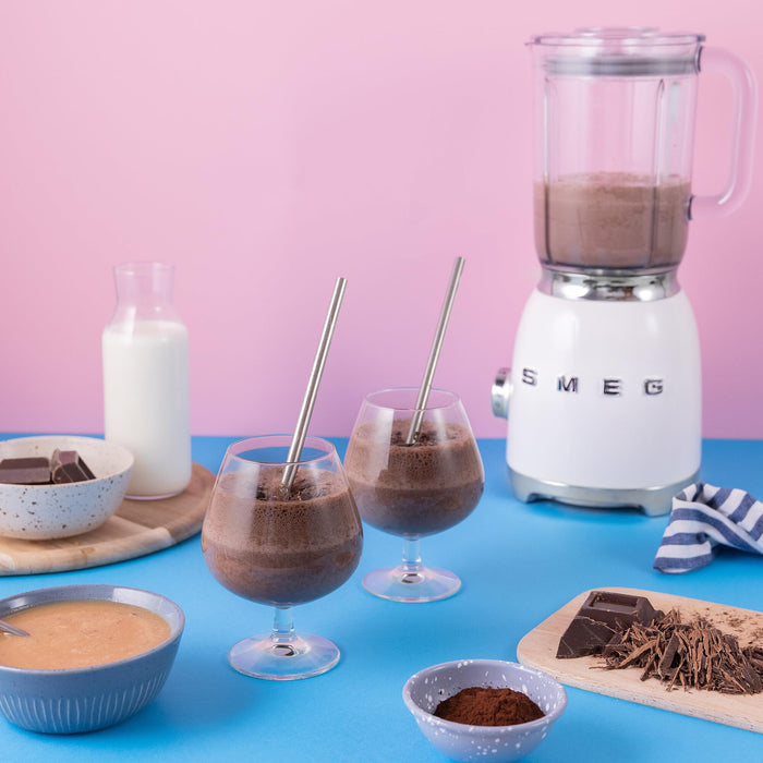 Chocolate smoothie preparation with Smeg blender on a blue table against a pink background