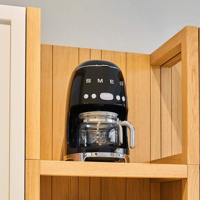 Black Smeg coffee machine placed on a wooden shelf