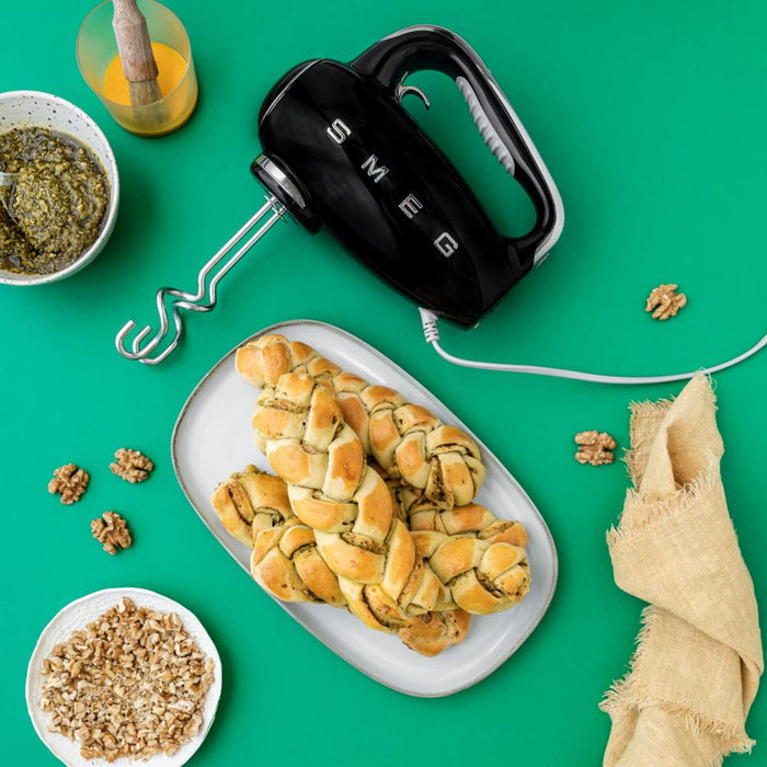 Black Smeg hand mixer on a green background with bread and ingredients