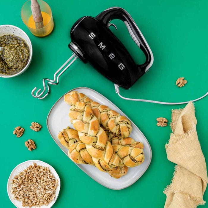 Black Smeg 50s retro line hand mixer next to pesto and pesto bread on a grean surface
