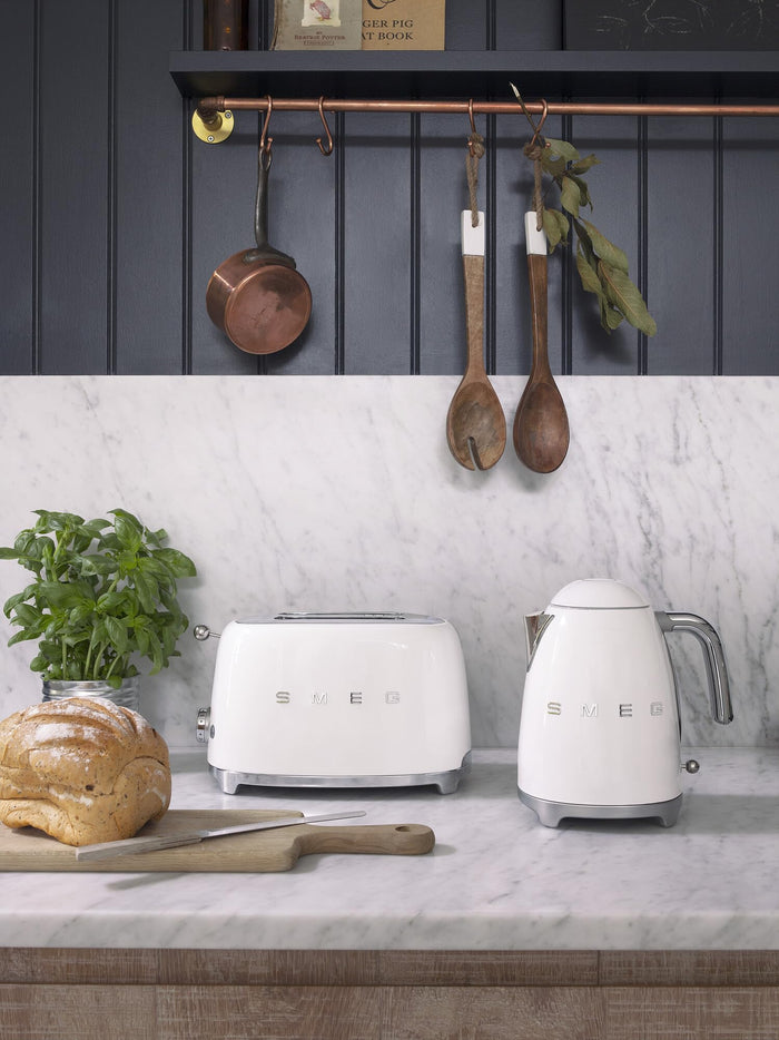 White toaster and kettle on a kitchen counter with a plant and bread loaf.