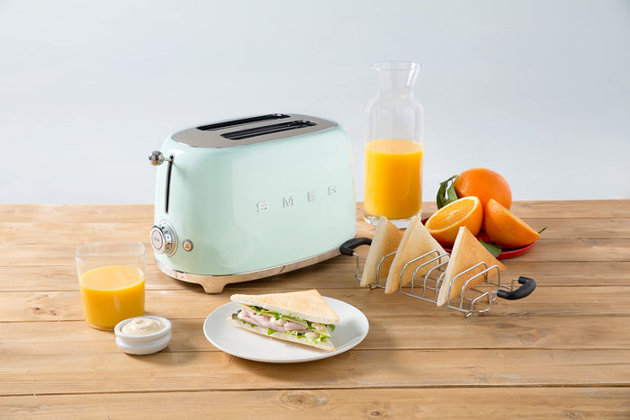 Mint green toaster on a wooden table with orange juice, toast, and fruit.