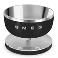 A SMEG branded digital kitchen scale with a modern matte black finish and a detachable stainless steel bowl.