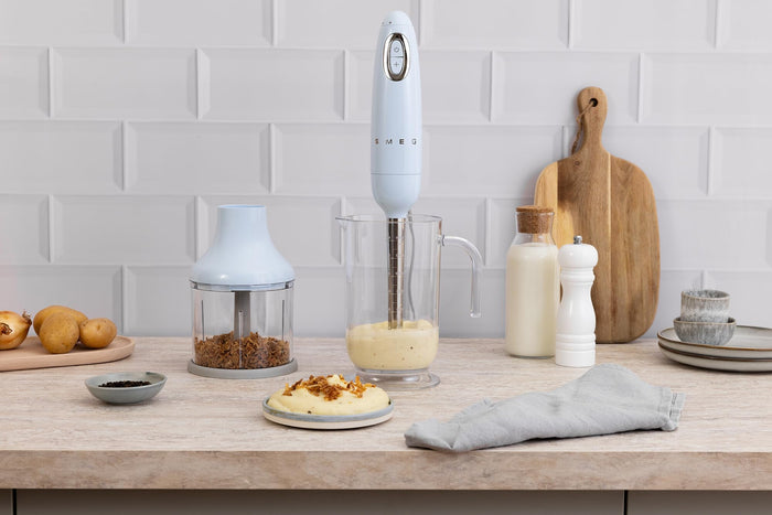 Smeg hand blender on a kitchen counter with various items including a cutting board and food.