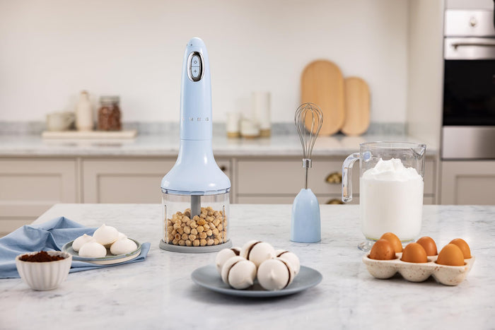 Handheld food chopper on a kitchen counter with various ingredients and kitchen tools.