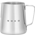 A SMEG branded stainless steel milk frothing jug with a handle and logo visible on the side.